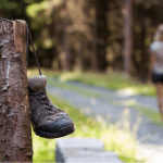 hiking boots hanging on fence post and person walking down the trail in the distance