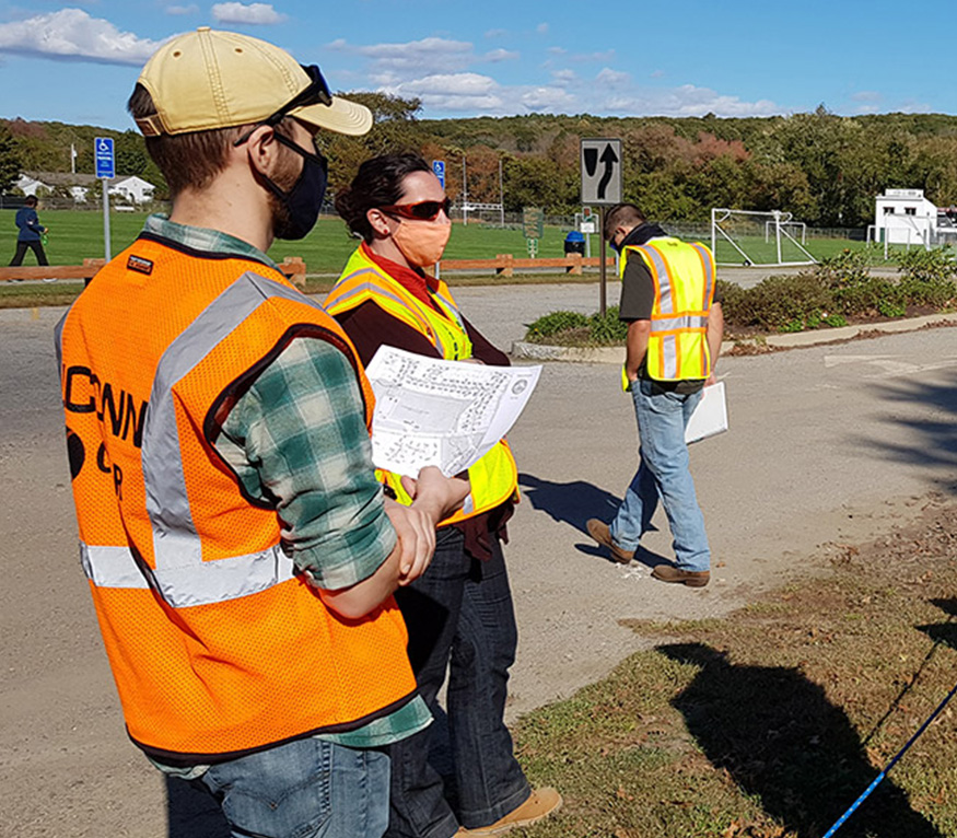 people reviewing a map outside at a town park wearing orange and yellow safety vests