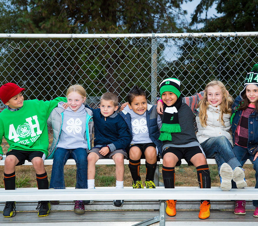group of smiling youth sitting on a bench at a sports field with fence behind them