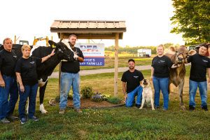 Hyde Dairy owners and employees with two cows in front of the farm sign