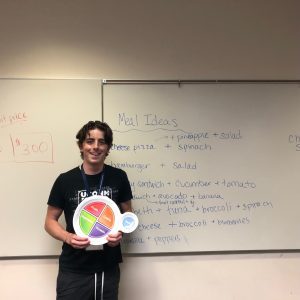 Riley holding a MyPlate in front of a white board with nutrition tips