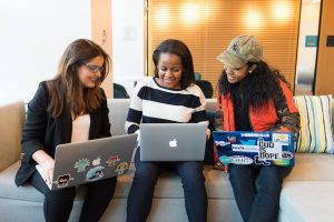three teen girls sitting on couch with laptops