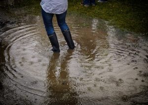 person wearing tall rain boots standing in a muddy puddle