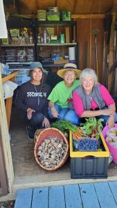 three women in a shed with vegetables and blueberries harvested from garden