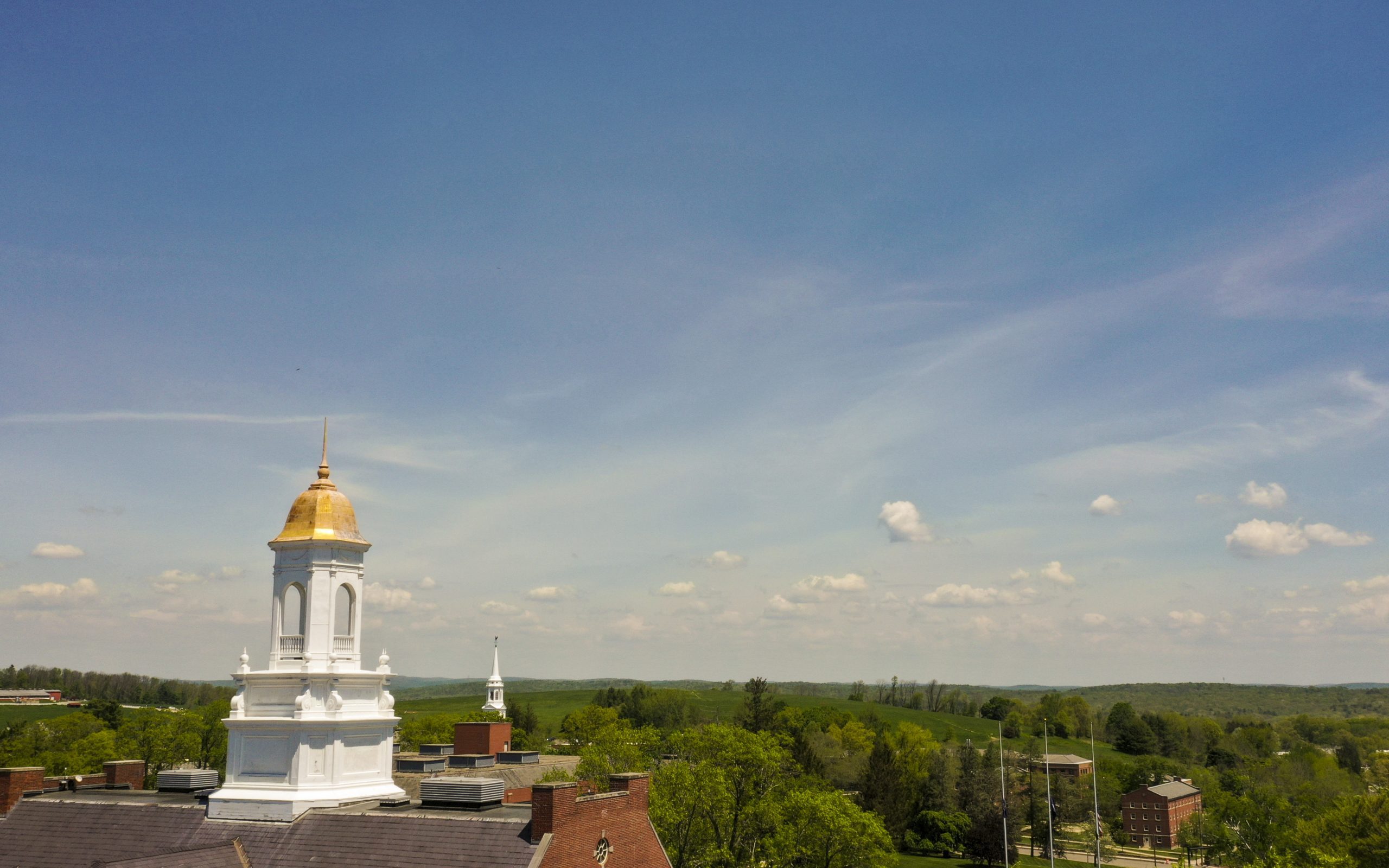 aerial view of the gold dome on UConn's Wilbur Cross building with blue sky and green hill in the background