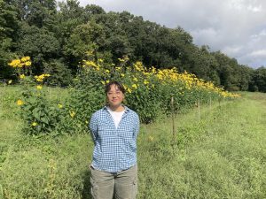 Maggie Ng standing in a field with yellow flowers behind her