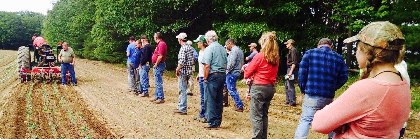 people standing around a tractor plowing a field 