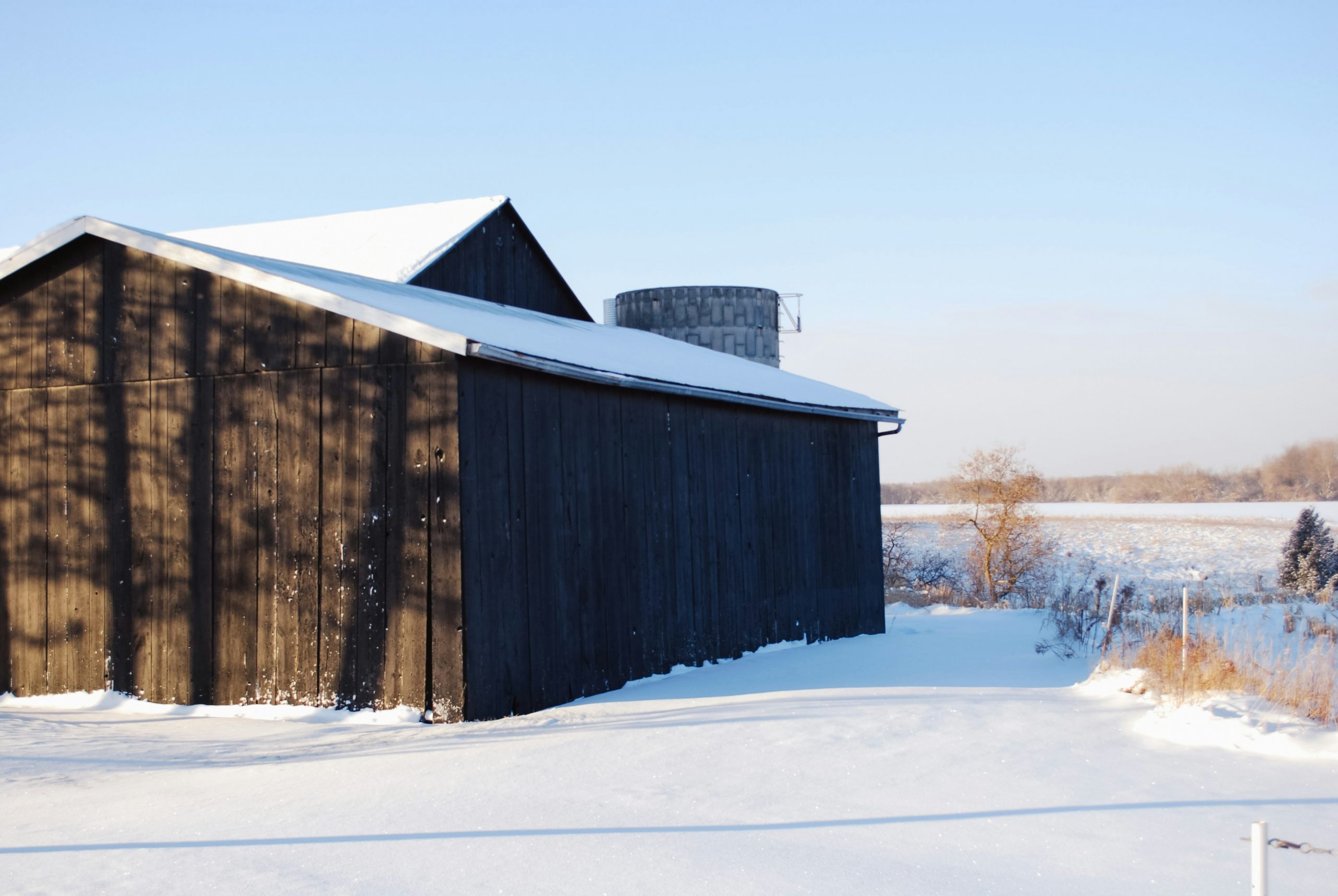 a barn and field in the snow with snow on the barn roof and the adjacent barn roof