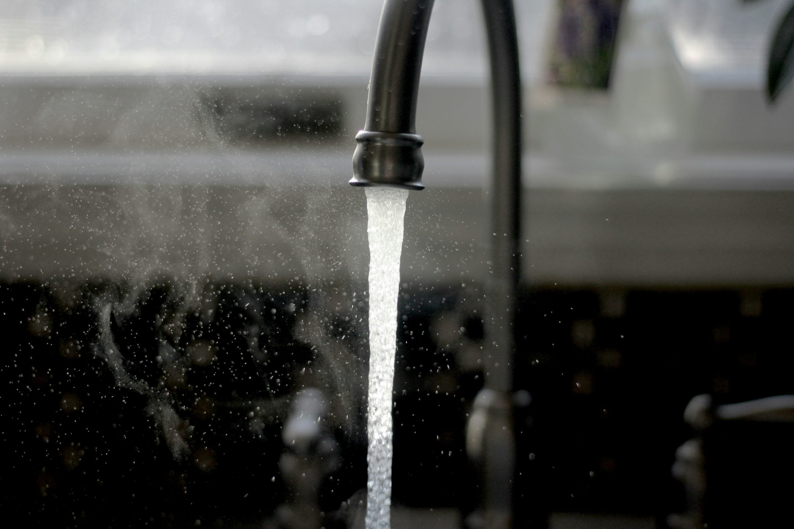 water running out of a kitchen faucet with droplets in the air