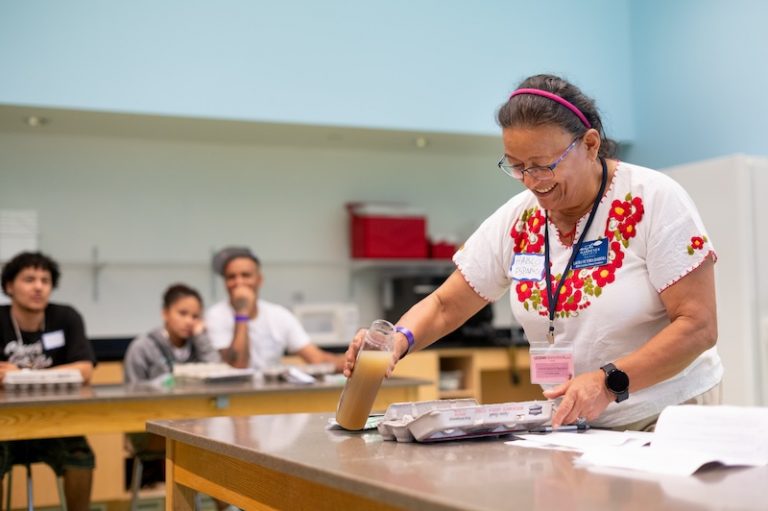 woman at a table demonstrating garden technique with three youth at a table in the background