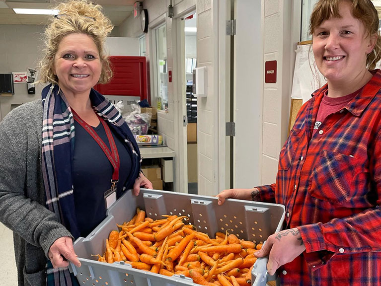 two women holding a bin of carrots