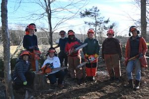 group of people with chainsaws smiling and wearing orange hard hats