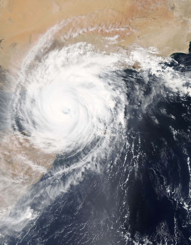 A satellite image of a typhoon over the Earth's surface, travelling over the ocean and desert landscape.