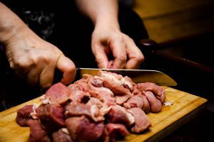 A man using a knife to cut raw meat on a wooden chopping board. (Usman Yousaf / Unsplash)