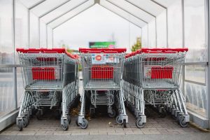 A clear hut in a parking lot with three rows of multiple silver and red shopping carts.