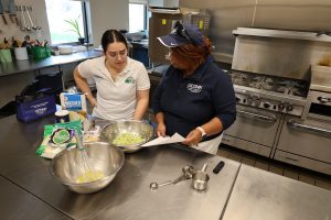 two people standing in a kitchen looking at a recipe