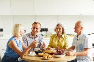 four people sitting at a kitchen table smiling and eating