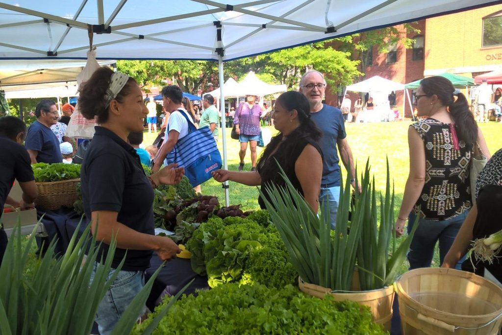 Women smiling at customers at a farmers market, with produce around her