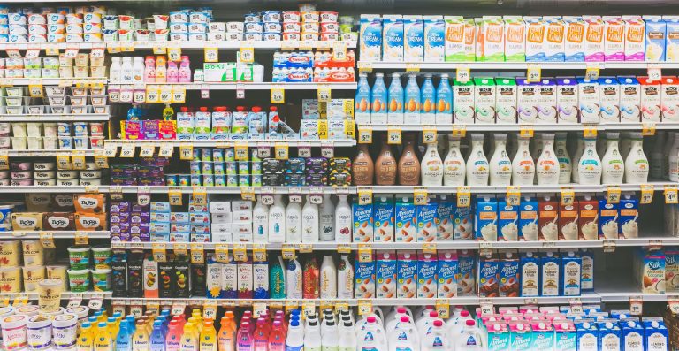 Image of a chilled dairy fridge in a supermarket. The shelves are filled with many different colored containers and bottles. (Kenny Eliason/Unsplash)