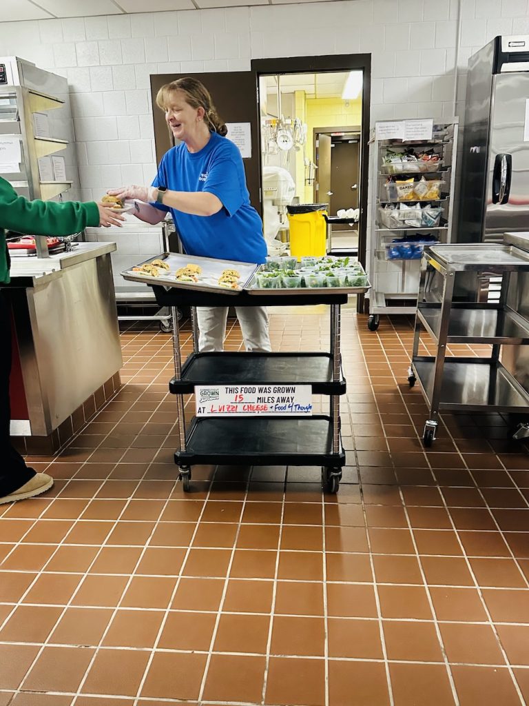 teacher handing a student a cup of arugula
