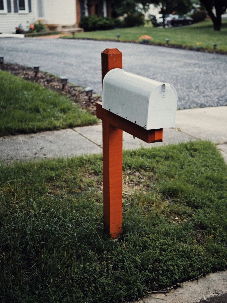 mailbox at the end of a driveway with a sidewalk and house in the background