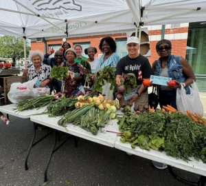 group of people standing under a CT Grown tent at a farmers market with vegetables in front of them