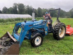 Jean Cardinale sitting on a blue tractor and waving