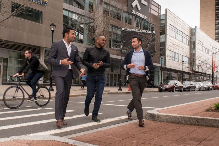 three young men in suits crossing a city street