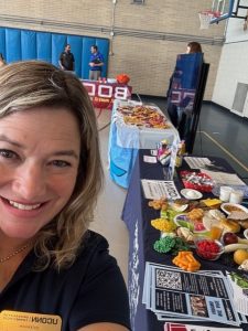woman in blue UConn Extension shirt taking a selfie in front of a food and nutrition education table at an event
