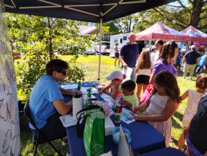 youth coloring at a table under a tent at a farmers market